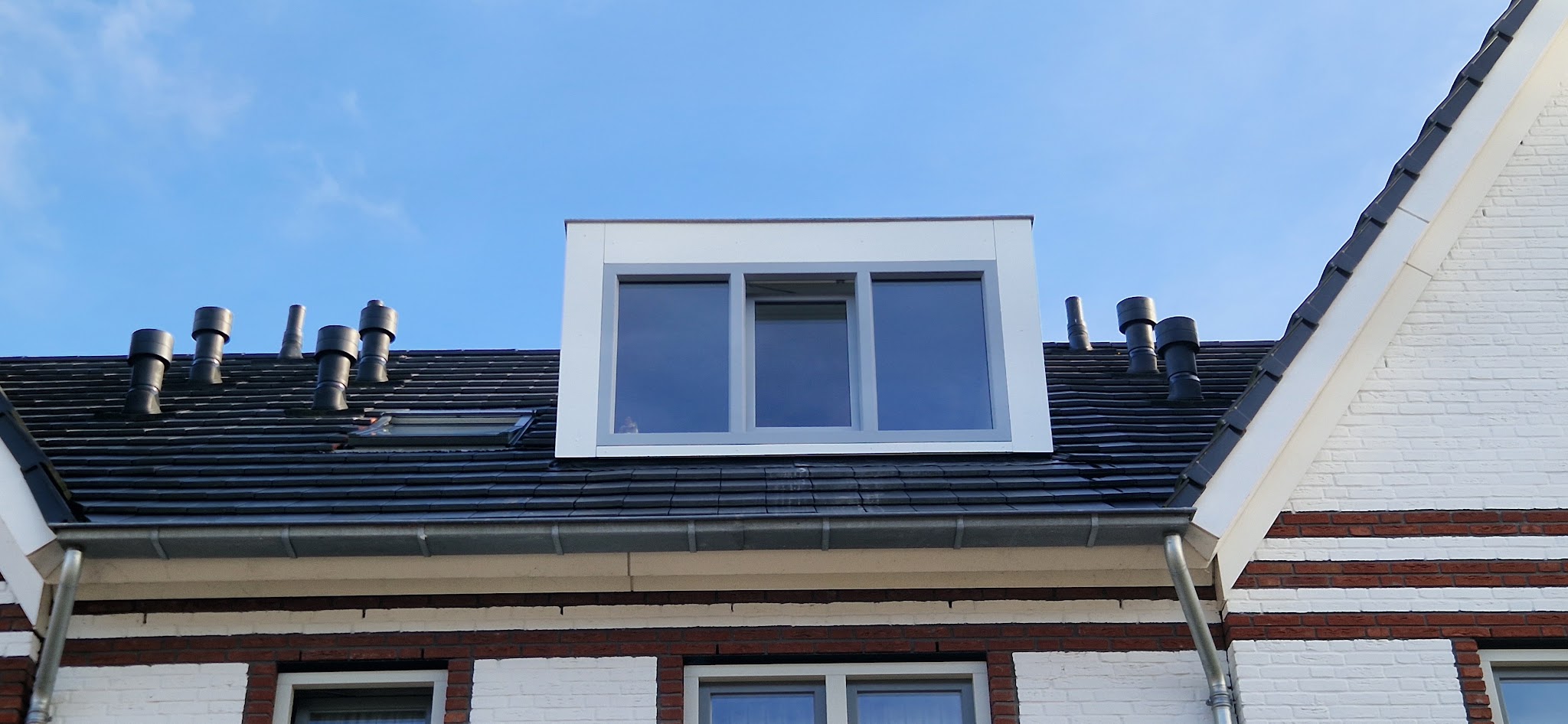 Witte dakkapel met drie ramen op een donker pannendak