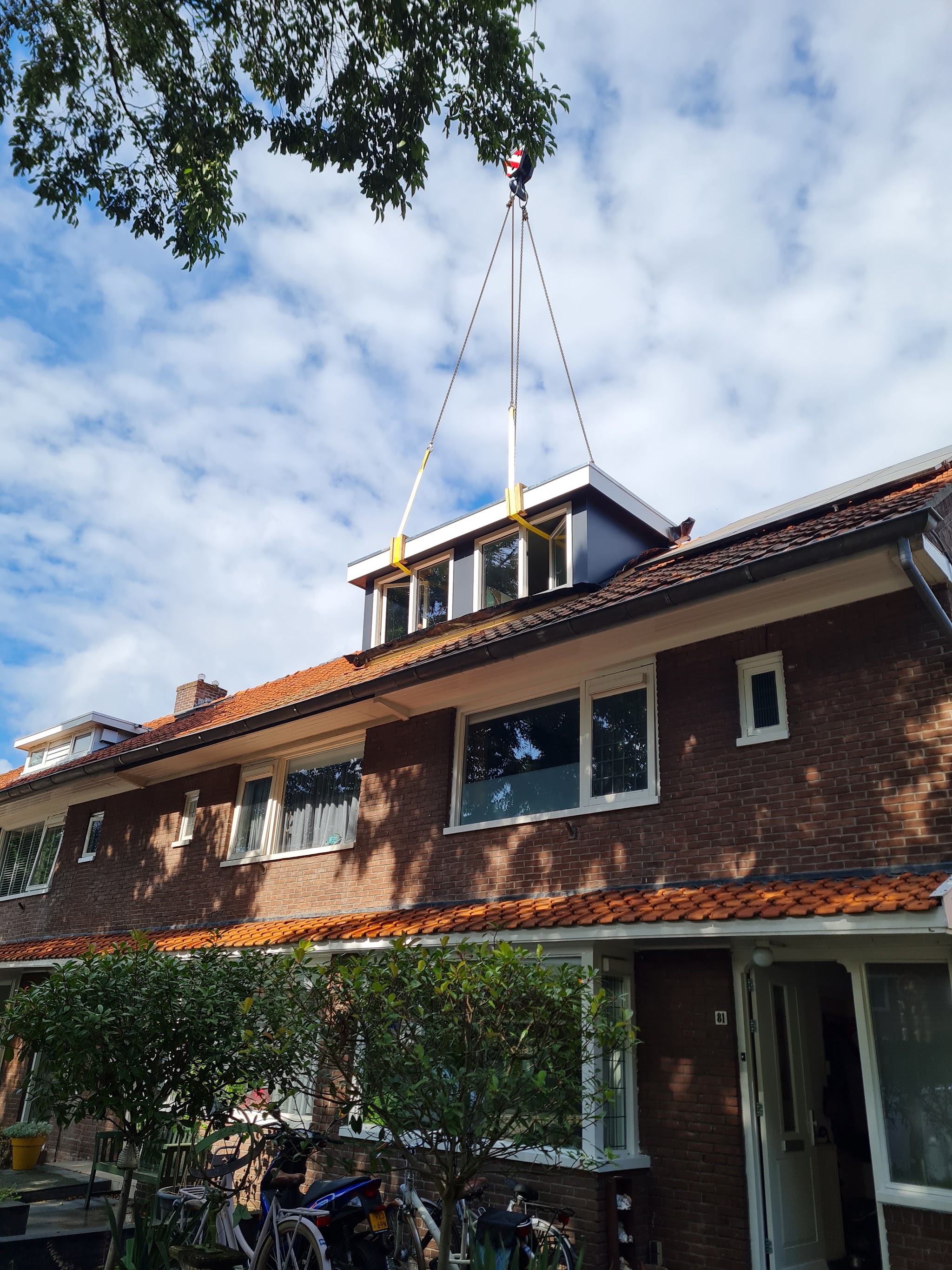 De complete dakkapel hangt aan de kraan boven een rij jaren dertig woningen